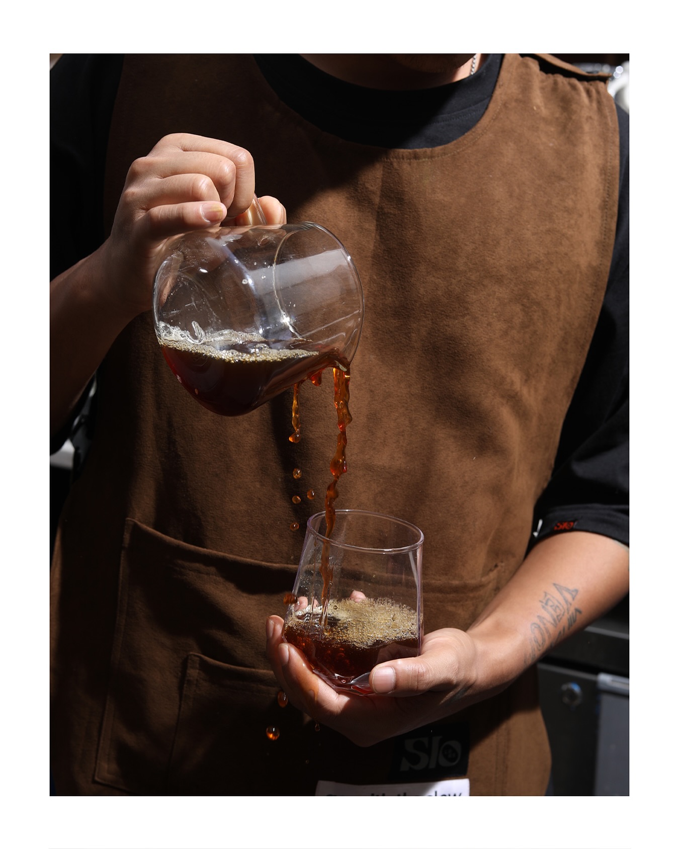 Slo Labs barista in brown apron pouring single-origin filter coffee from a glass carafe