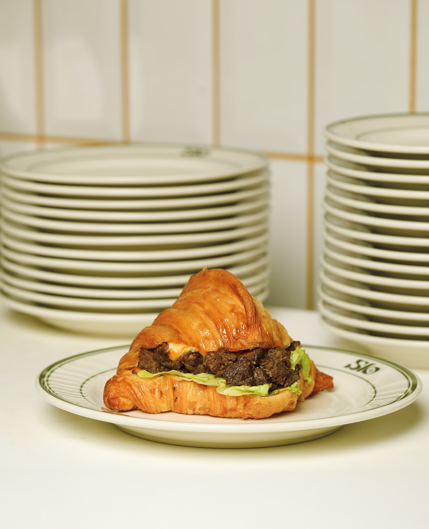 Slow-cooked beef croissant sandwich on a green-striped Slo Labs plate